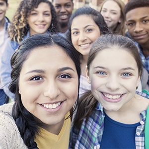 Diverse group of teens looking at camera taking selfie at high school Diverse group of eight high school students are smiling and looking at the camera. Teenagers are students at public high school, and are wearing backpacks or holding school books.