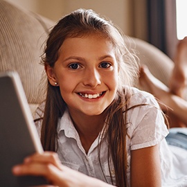 Full length portrait of a young girl using her tablet while lying on a sofa at home
