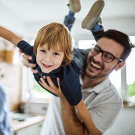 Happy little boy having fun with his father at home and looking at camera. There are people in the background.