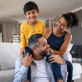 Happy ethnic family playing together at home Cheerful african mother and indian father playing with son at home. Cute boy enjoying sitting on father shoulder while looking at camera. Middle eastern family having fun together on the sofa at home.