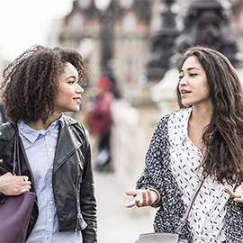 Two female friends talking outdoors in Paris, France Two young women walking in Paris street having conversation. Young woman gesturing with hands, female friend listening