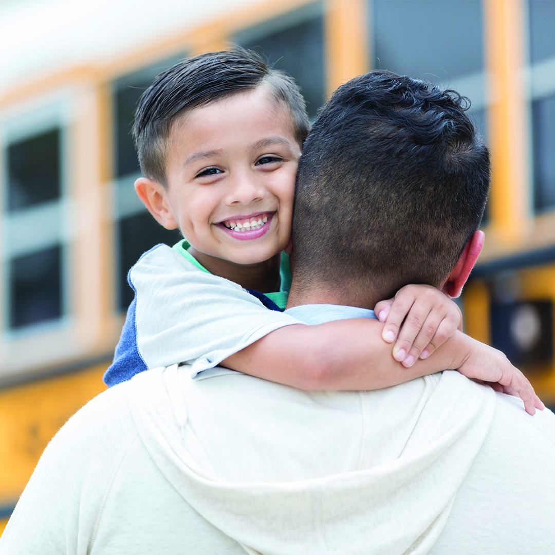 Schoolboy greets father after first day A confident little boy smiles for the camera as he embraces his father after the first day of school. He has just ridden the school bus home.