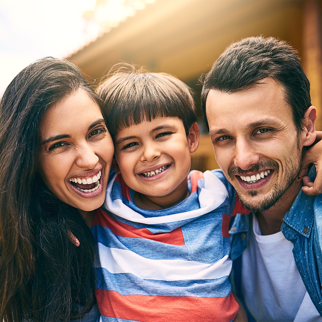 Cropped portrait of a happy young family of three sitting outside in their backyard